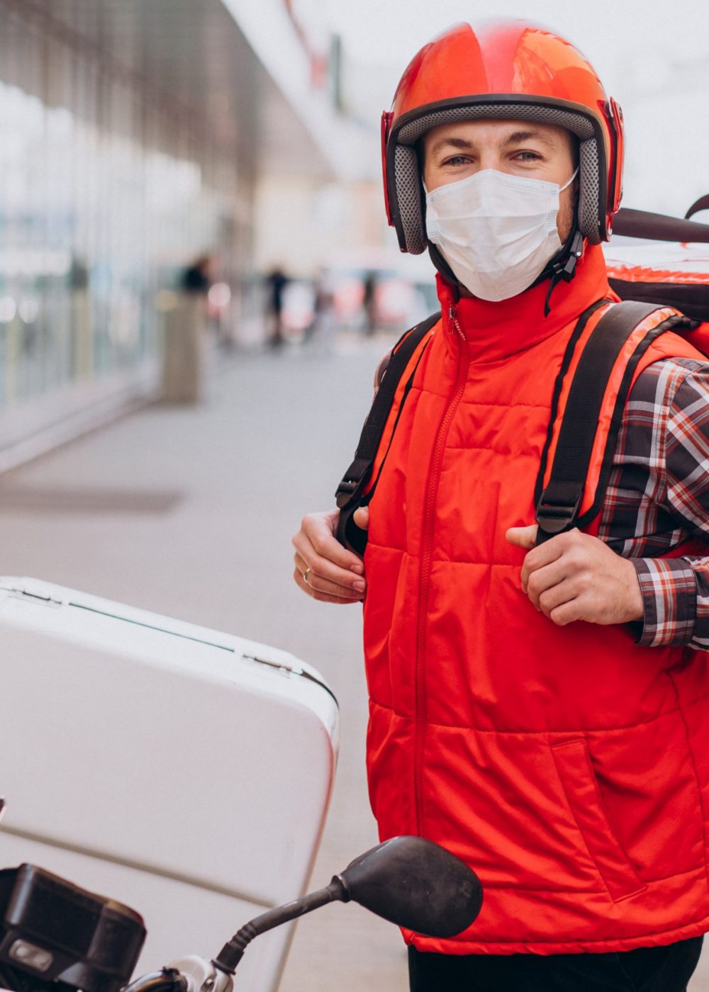 Food delivery boy driving scooter with box with food and wearing mask